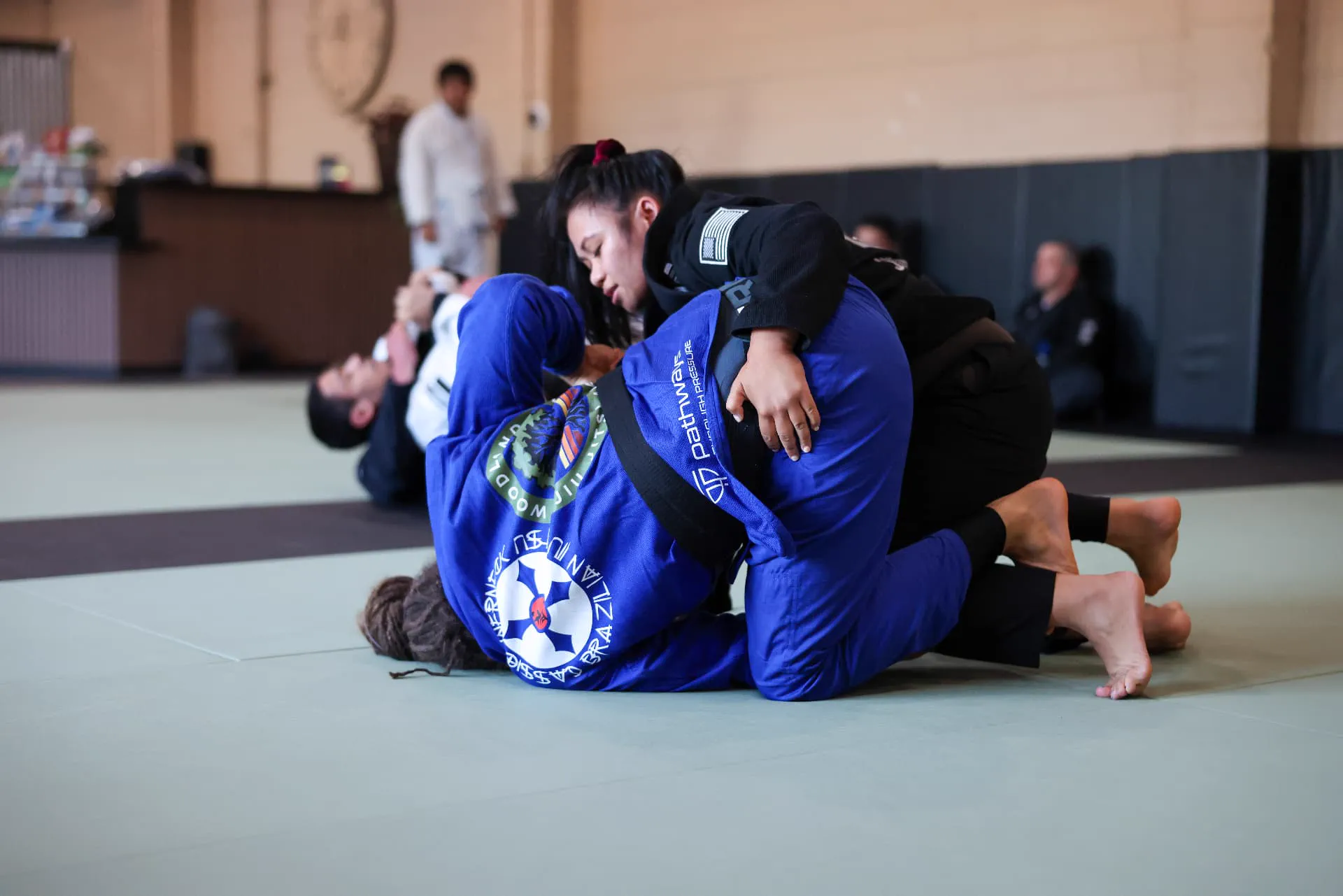 Two adult students sparring in blue and black gis during an evening Jiu-Jitsu class